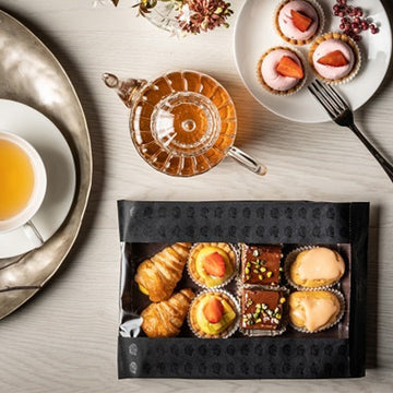 Tavolino visto dall'alto con tazza di te piatti di pasticcini e busta nera con finestra piena di pasticcini